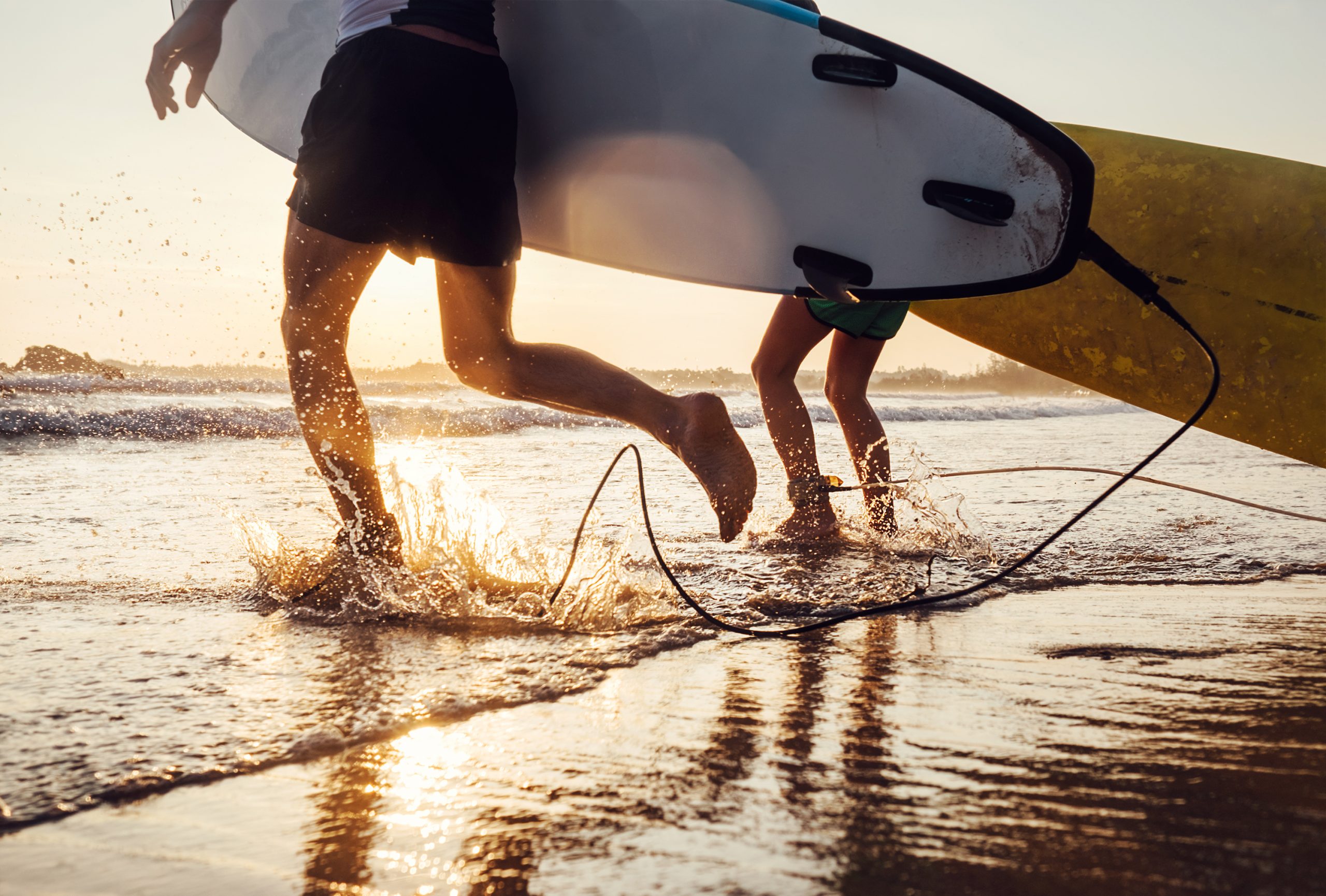 Surfers running into the sea at sunset